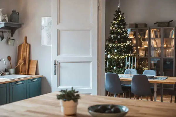 Julstämning i köket med en öppen dörr som avslöjar ett vackert julpyntat träd och en matsal. Perfekt jul inredning inspiration.