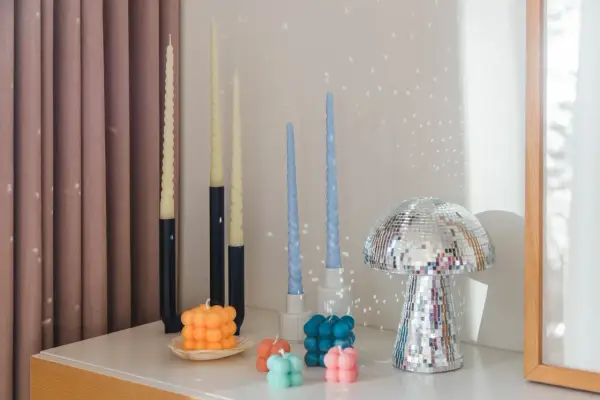 En samling av DIY ljus i olika former och färger, inklusive bubbel- och vridna ljus, samt en glittrig svampformad dekoration.