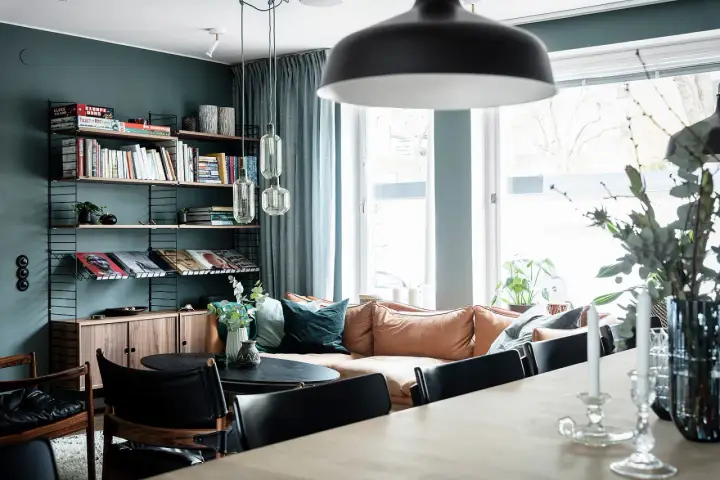 Vardagsrum med bokhylla i 50-talsstil, soffa i läder och stora fönster.